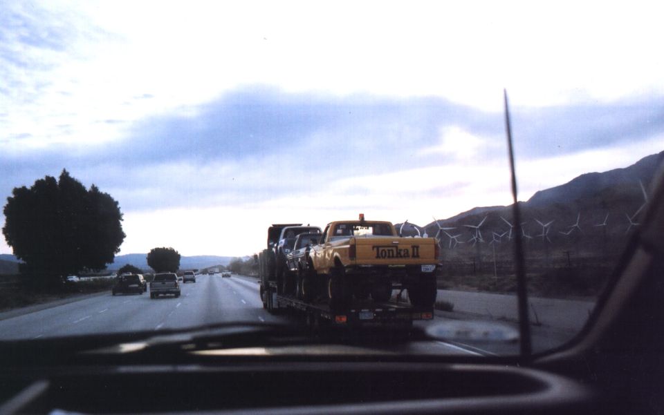 Yellow lifted Ford pickup lettered Tonka II hauled on a flatbed trailer down a freeway