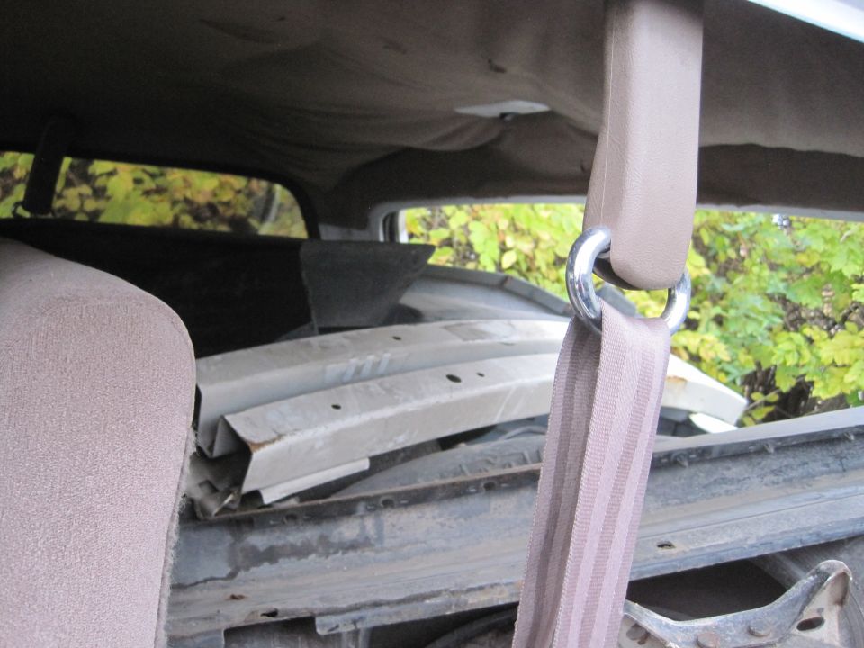 Close-up of a car's interior seatbelt mechanism and strap, with damaged car parts visible through the rear window.