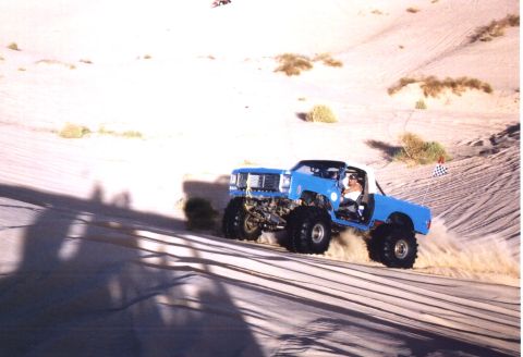 2000 Ford F-450 - A lifted blue square-body Chevrolet/GMC pickup with a white roll bar, no doors, and oversized paddle-style off-road tires on white wheels c…