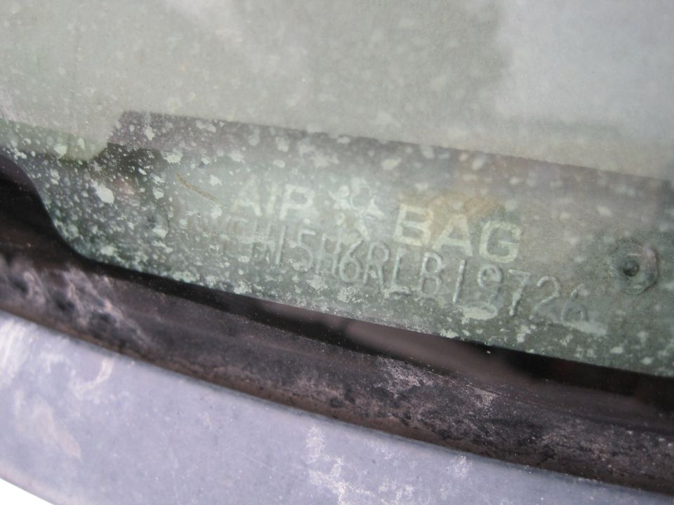Close-up of a weathered VIN sticker on a car windshield with text "AIR BAG" and partial VIN "H5H6RLB19726".