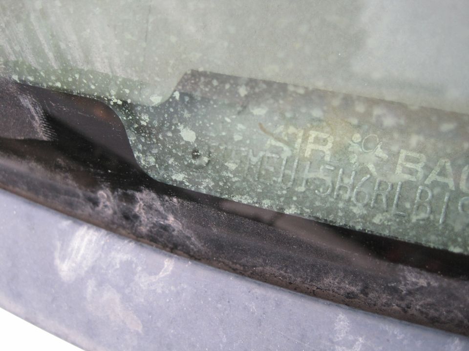 Close-up of a VIN plate on vehicle glass with visible corrosion.