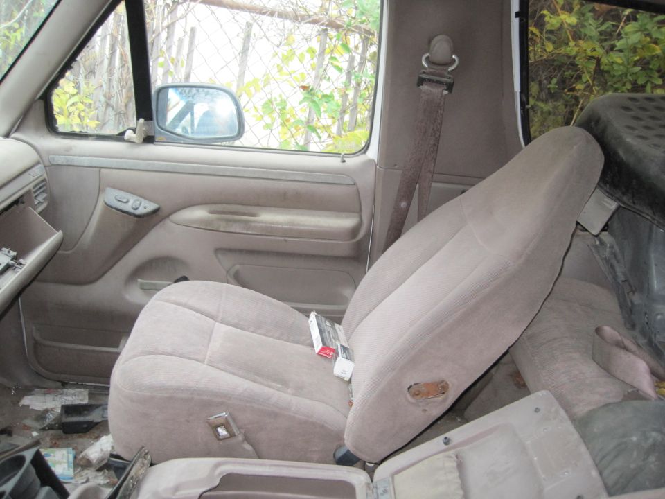 Interior of a dirty vehicle showing a tan cloth seat with cigarettes on it.