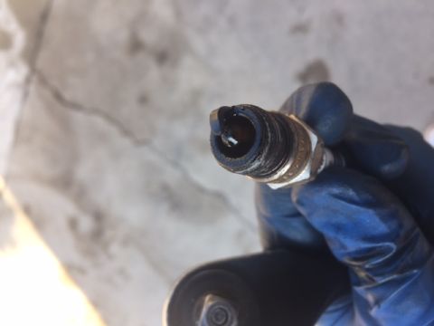1978 Ford Bronco - A gloved hand holds a dirty spark plug with a damaged electrode. The spark plug appears to be from a vehicle's engine.