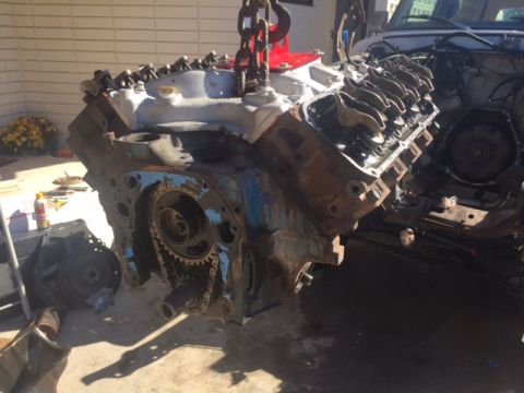 1978 Ford Bronco - A V8 engine block, likely from a classic American vehicle, is suspended by a red engine hoist. The engine shows signs of rust and wear, wit…