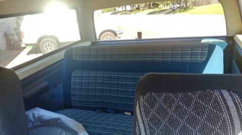 1984 Ford Bronco - View from the back seat of a white SUV, looking out the rear window at another vehicle parked outside.