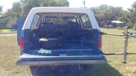 1984 Ford Bronco - Rear view of a blue SUV with a white top, showing the open cargo area and a spare tire.