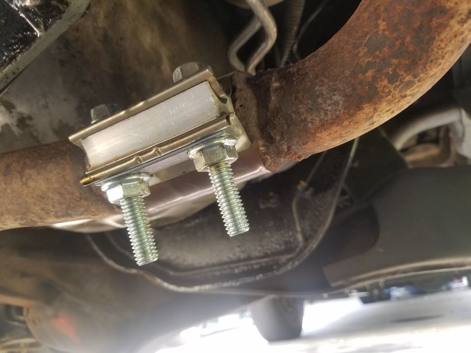 Exhaust pipe hanger with two bolts attached to a rusty pipe