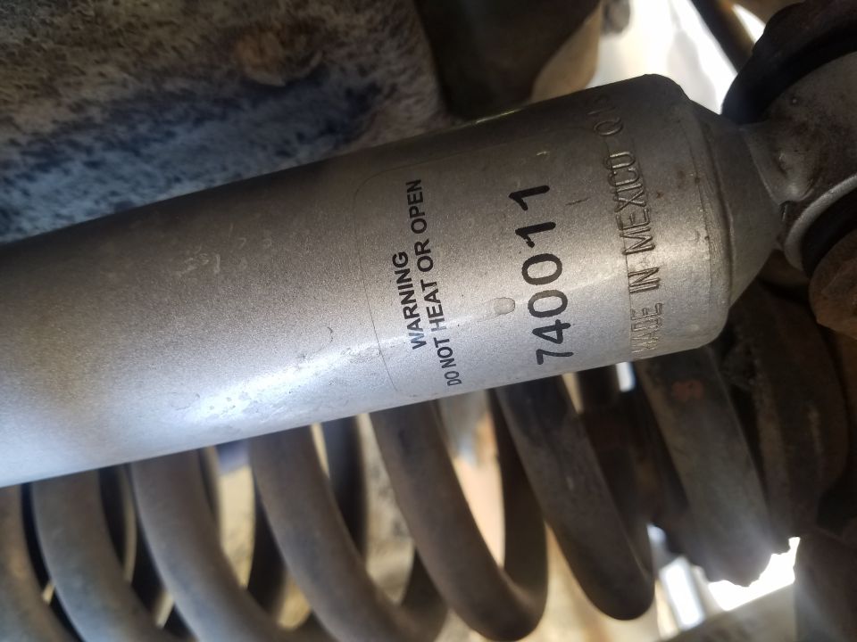 Silver shock absorber with warning label and part number 740011 above a coiled spring.