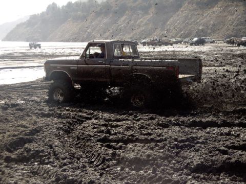2000 Ford F-450 - A lifted late-1970s Ford short-bed pickup blasting through a churned mud pit, throwing clods of mud into the air behind the rear tire. The…