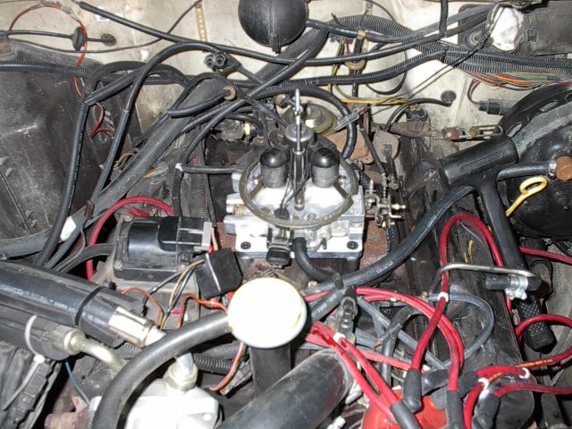 Engine bay showing a carburetor, spark plug wires, and various hoses and electrical connections