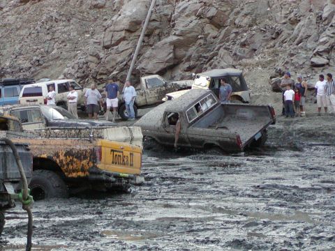 2000 Ford F-450 - Mud-splattered trucks bogged in a canyon mud pit below a rock face: a yellow pickup with 'Tonka II' on the bedside sits caked in mud at lef…