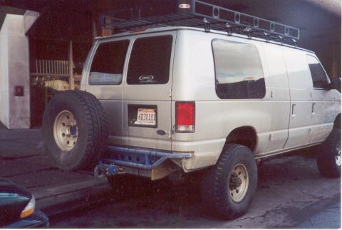 1995 Ford Bronco - Silver Ford Econoline van equipped with a roof rack and rear-mounted spare tire.