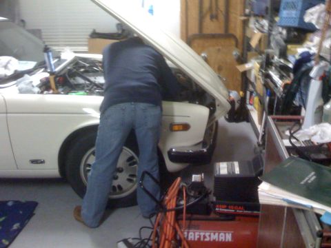1987 Jaguar XJ6 - Mechanic attends to the engine bay of a 1987 Jaguar XJ6 in a cluttered garage setting.