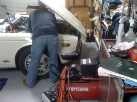 1987 Jaguar XJ6 - A person is working on the engine of a white car in a cluttered garage setting.
