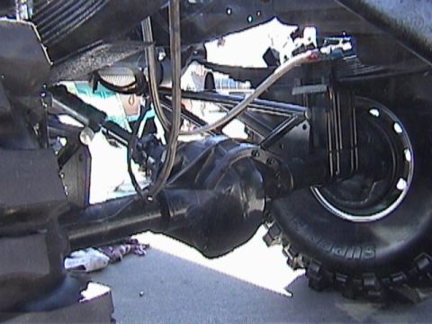 1995 Ford Bronco - The underside of a vehicle shows its rear axle, suspension components, and a large tire. A website logo is visible at the bottom right.