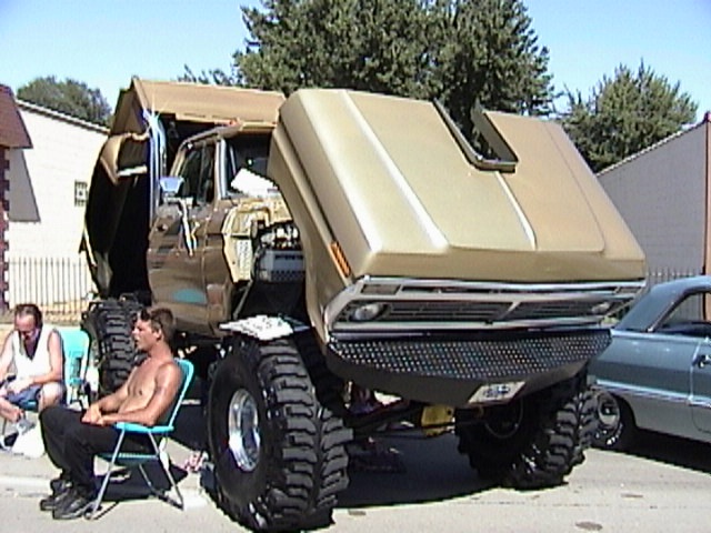 Gold custom monster-truck Ford on huge tires with hood up in a driveway