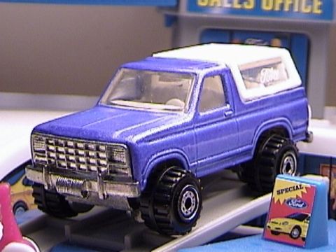1979 Ford Bronco - A blue 1978 Ford Bronco toy with a white top is displayed on a ramp in front of a toy sales office.