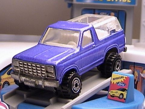1979 Ford Bronco - This blue 1979 Ford Bronco toy features a clear top and off-road tires, presented on a toy service ramp.