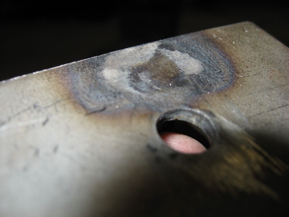 Finger poking through a hole in a discolored piece of metal.
