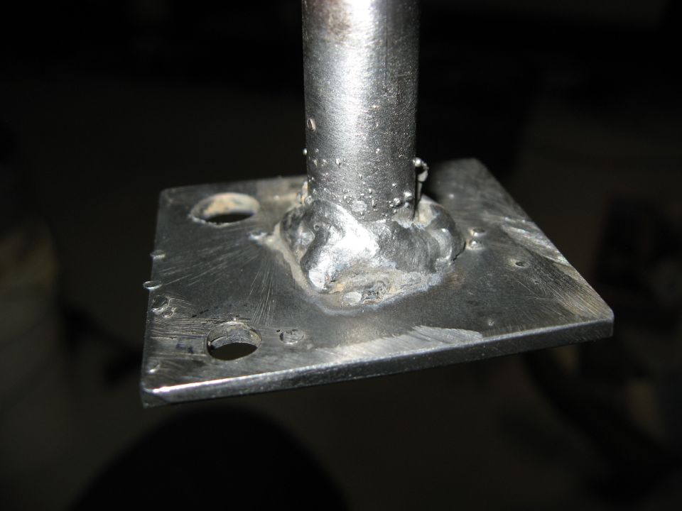 Close-up of a metal plate with a welded post and two holes.