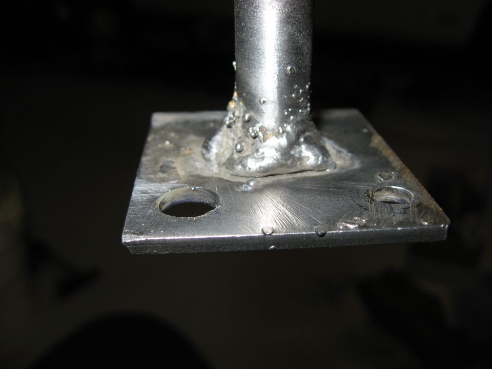 Close-up of a metal plate with a welded post and two drilled holes.
