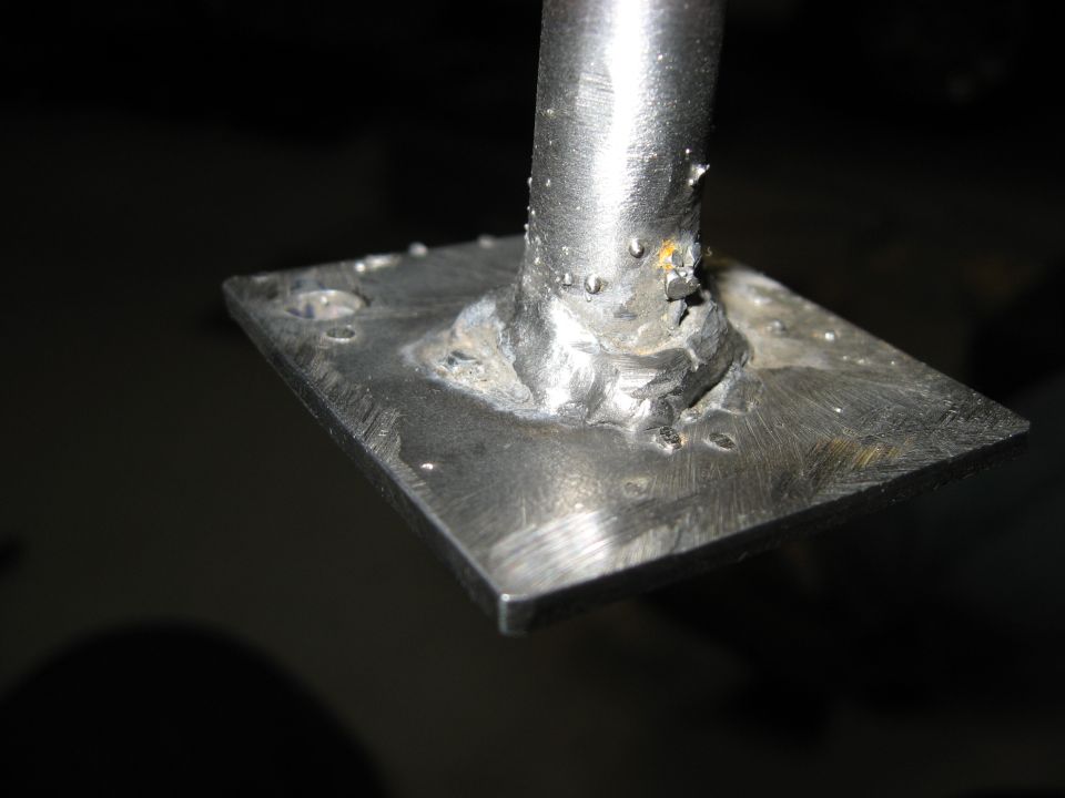 Close-up of a rough metal weld attaching a post to a square plate.