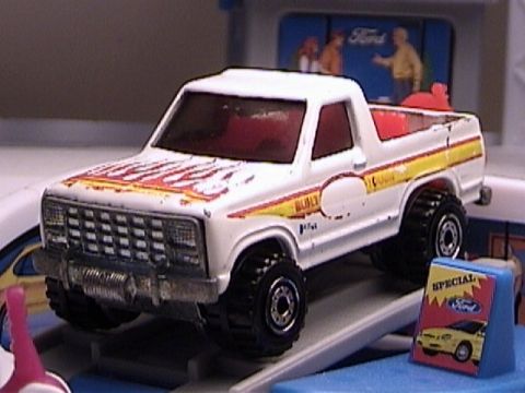 1979 Ford Bronco - A white toy Ford Bronco with flame graphics and "BUILT TOUGH" text is displayed on a ramp.