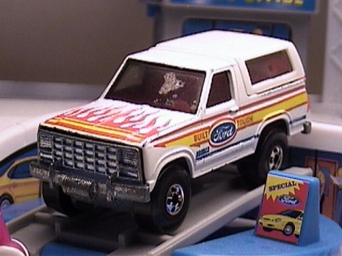 1979 Ford Bronco - A white toy Ford Bronco with flame decals and "Built Ford Tough" text is displayed on a ramp.