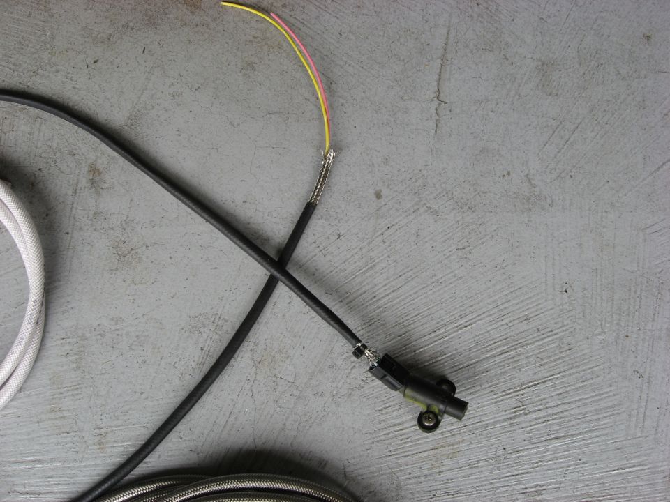 Black automotive wire harness with exposed yellow and pink wires on gray concrete.