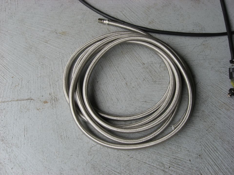 Coiled stainless steel braided hose and black cable on concrete