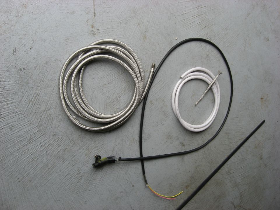 Automotive parts including hoses, cables, and a rod on a concrete surface.