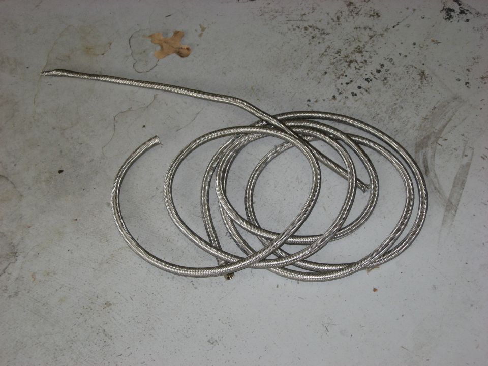 Braided metal hose coiled on concrete with a dry leaf