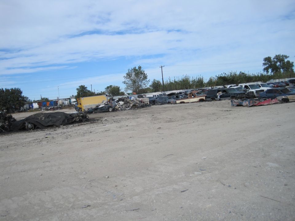 Junkyard with wrecked vehicles, including a yellow truck and car bodies.