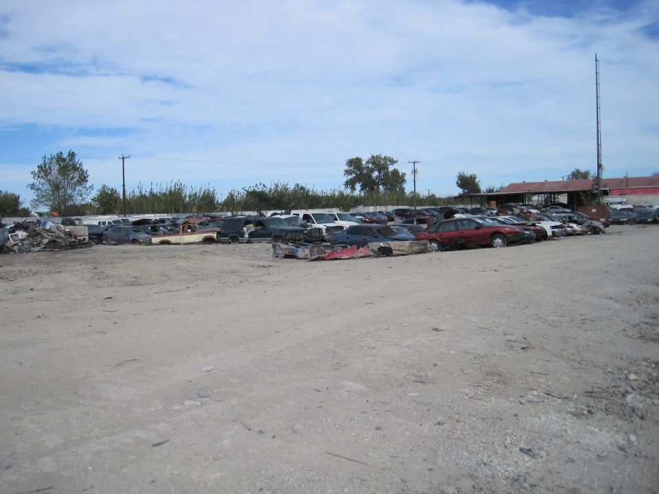 Junkyard with many wrecked cars parked on a dirt lot.