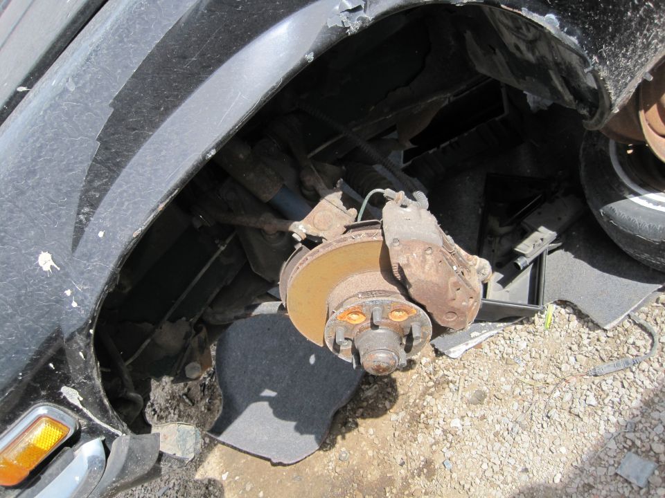 Close-up of damaged Jaguar XJ6 wheel well with rusty brake rotor and caliper.