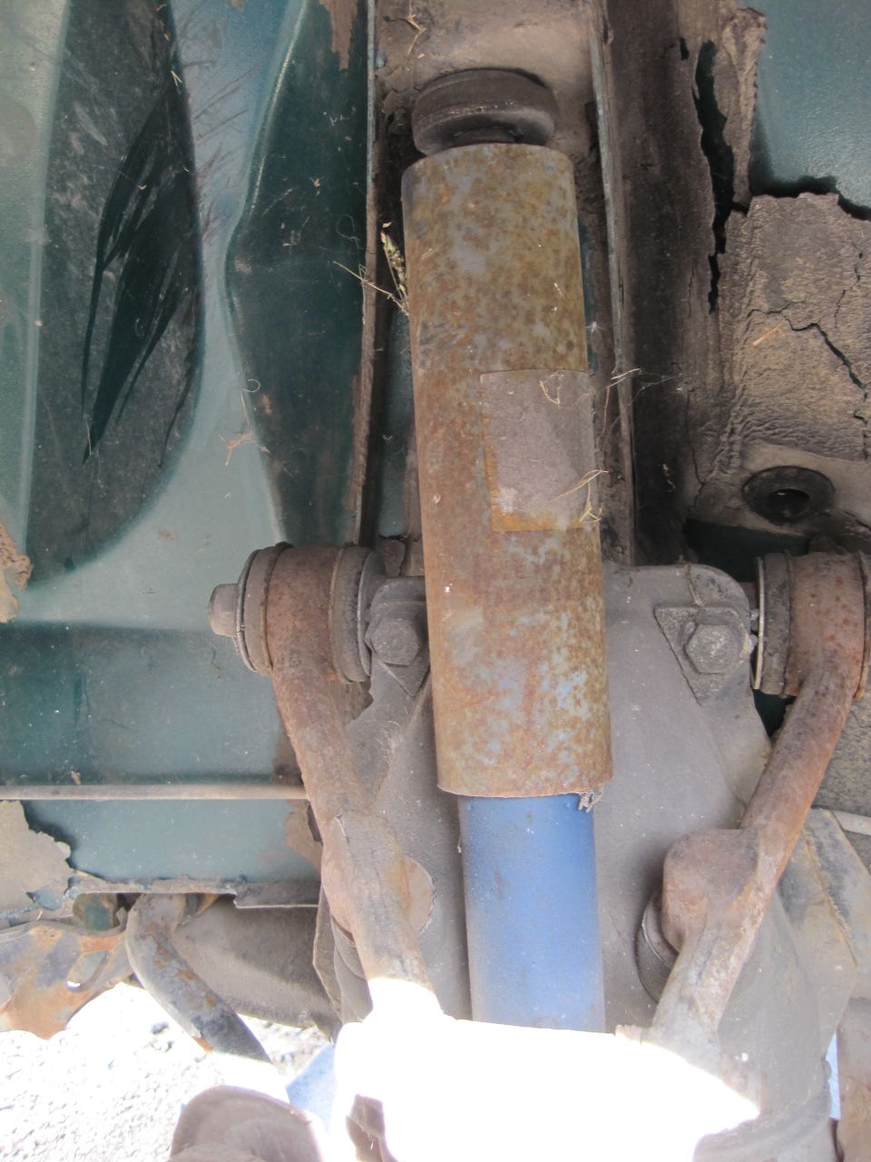 Rusty shock absorber with blue boot on vehicle suspension