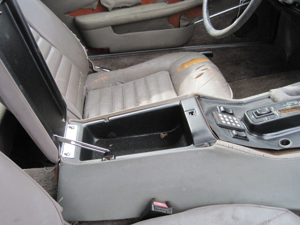 Interior of a vintage car showing a gray center console with an open storage compartment and electronic controls.