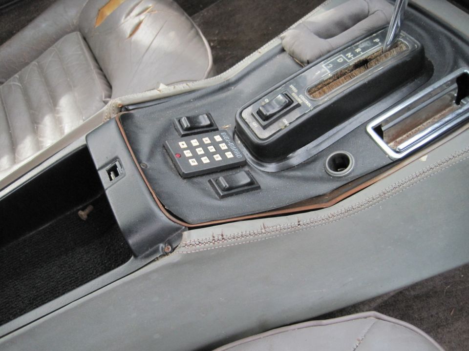 Center console of a vintage car with gear shifter, keypad, and storage compartment.