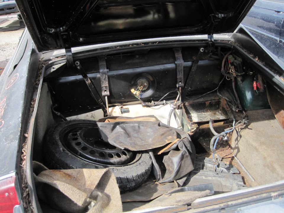 Open trunk of a Jaguar XJ6 showing spare tire, fuel tank, and wiring.