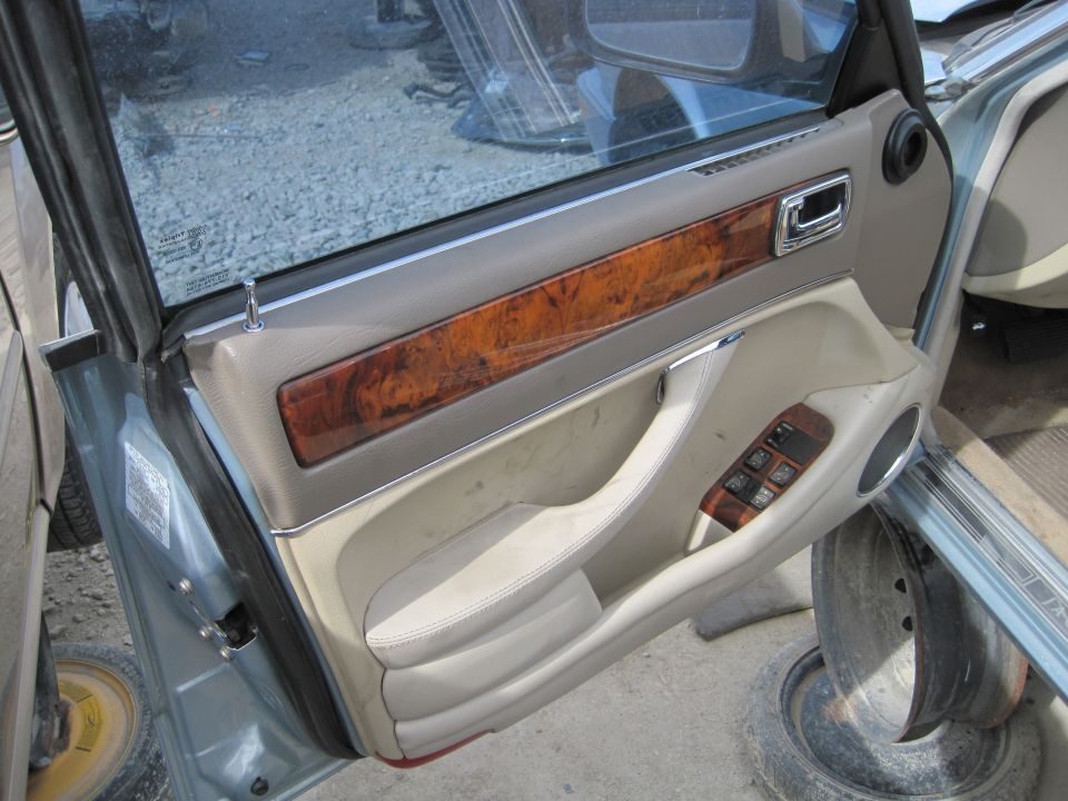 Interior door panel of a light blue Jaguar XJ6 with wood trim and power window controls.