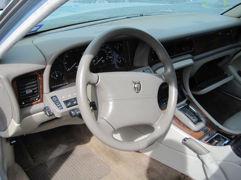 Interior of a beige 1985 Jaguar XJ6, showing steering wheel, dashboard, and center console.