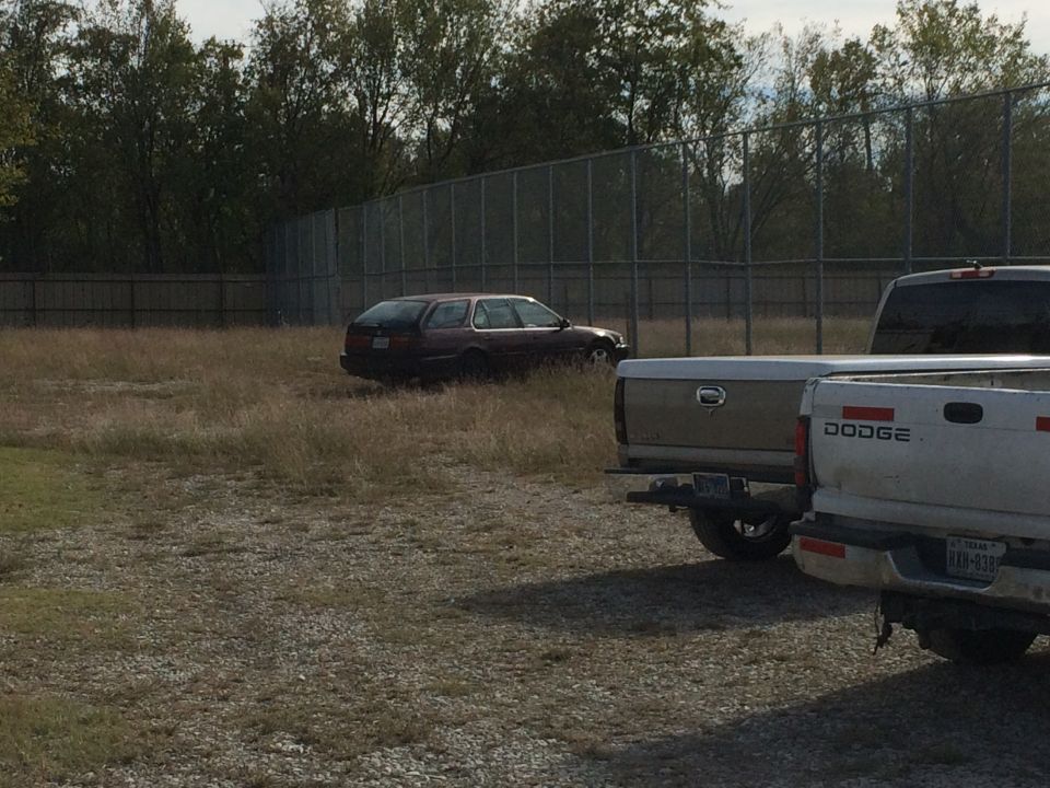 Dark red station wagon in a field with two pickup trucks in the foreground.