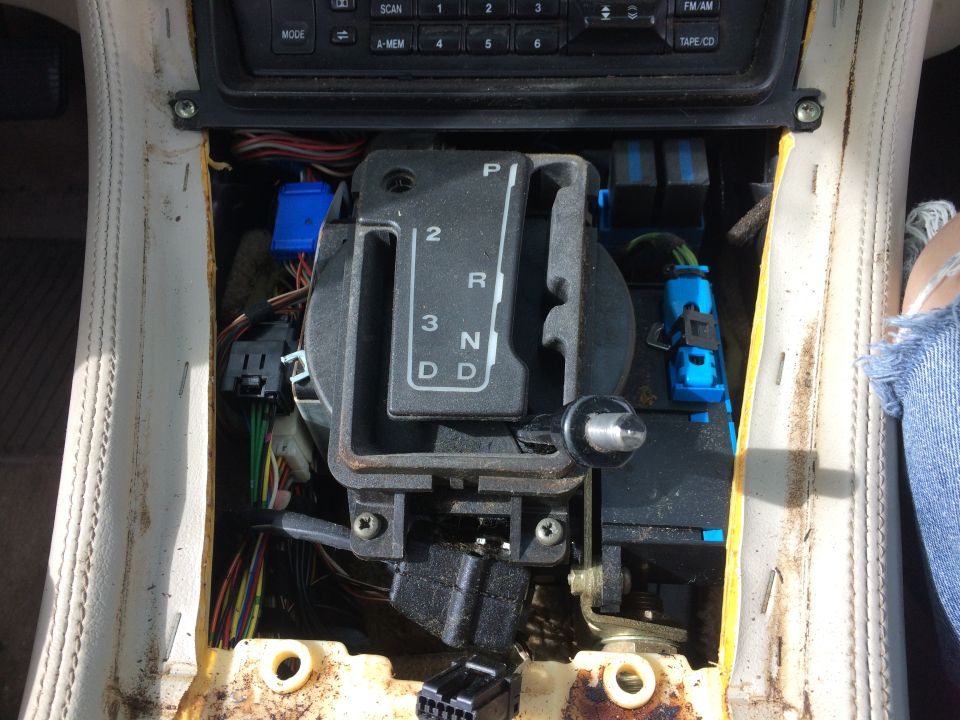 Disassembled car center console with gear shifter and exposed wiring.