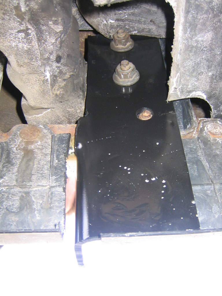 Black metal bracket with rusty bolts under a vehicle frame