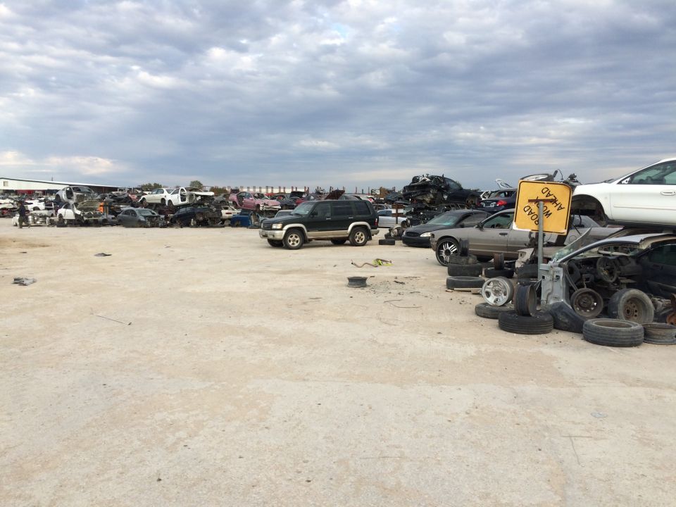 Junkyard with many wrecked cars, a "WORK AHEAD" sign, and a cloudy sky.