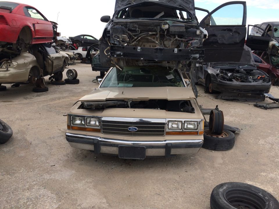 Junkyard scene with a tan sedan in the foreground and another car stacked on top.