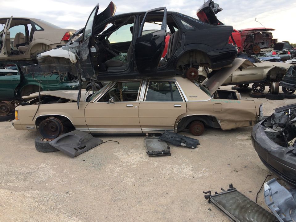 Junkyard with stacked cars, including a tan sedan and a black sedan on top.