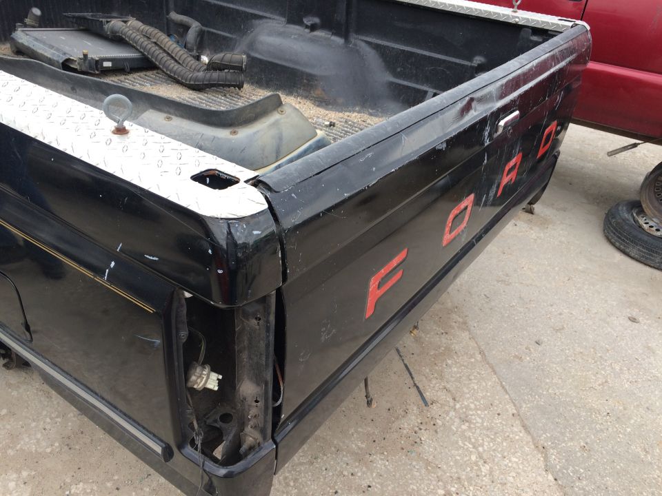 Black pickup truck bed corner with red FORD lettering and diamond plate accent.