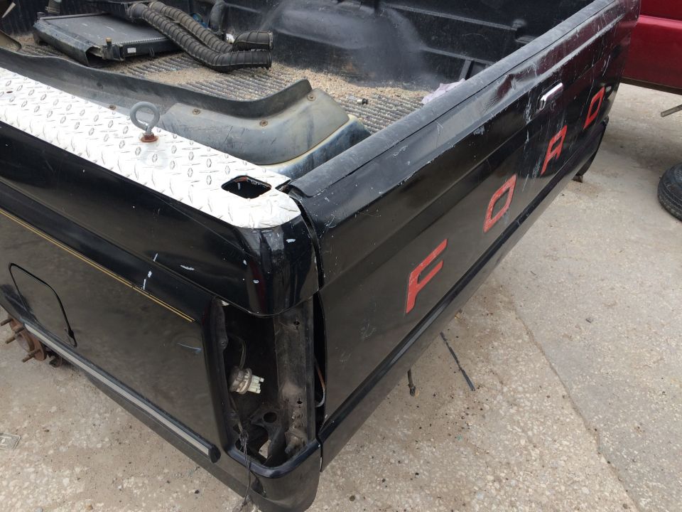 Black pickup truck bed with red 'FORD' lettering, missing taillight, and diamond plate trim.