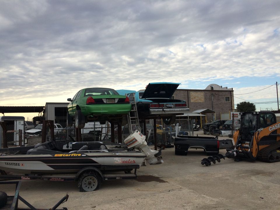 Green sedan on lift, boat on trailer, bulldozer in junkyard.